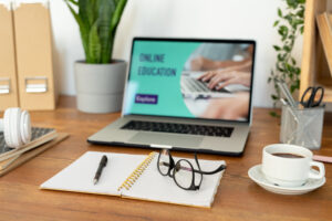 Laptop na biurko, przed nim notatki z długopisem i okularami. Na ekranie widać CRM dla firm szkoleniowych, które prowadzą szkolenia online.